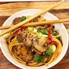 a white bowl filled with noodles, mushrooms and veggies next to chopsticks