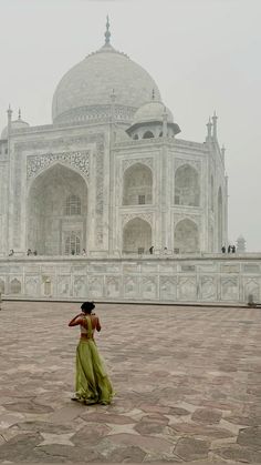 a woman standing in front of a large white building with a clock on it's side