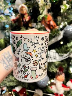 a person holding up a coffee mug in front of a christmas tree with ornaments on it