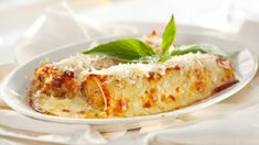 a white plate topped with lasagna covered in cheese and basil leaf garnish