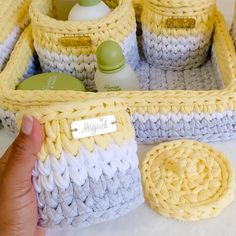 a hand holding a yellow and white crochet basket with soap, lotion and other items in it