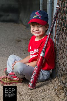 a young boy sitting on the ground with a baseball bat in his hand and smiling