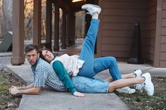 a man and woman laying on the ground in front of a house with their arms around each other