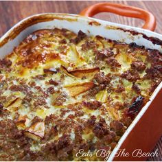 a casserole dish with meat and cheese in it on a wooden table next to an orange handled utensil