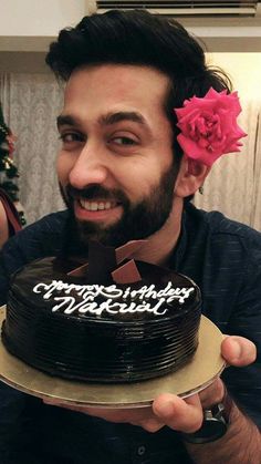 a man holding a chocolate cake with white frosting and a pink flower in his hair