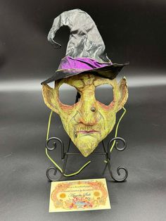 This papier-mâché witch mask is truly one-of-a-kind. Made with high-quality materials this mask is perfect as a decoration or can be worn by youth ages 7-12. If solely wanting to display this work of art, it can be tied from behind and hung directly on a wall, or displayed on a stand as shown. This can be used/worn/displayed not just for the Halloween season, but all year round. The face portion measures roughly 8" ~ not including the embellishments. (Hat, hair, etc.) Witch Mask, Hat Hair, Costume Masks, Costume Mask, Halloween Season, Dart, Costume Accessories, The Face, D Art