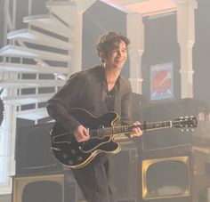 a man holding a guitar while standing on top of a stage