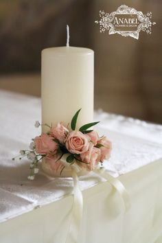 a white candle with some pink flowers on it and a ribbon tied around the candle