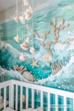 a baby crib with sea shells hanging from it's hooks in front of a mural