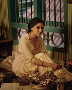 a woman sitting on the floor in front of a table with flowers and other items