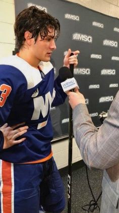 two men are talking to each other in front of a microphone while one man is wearing an orange and white jersey