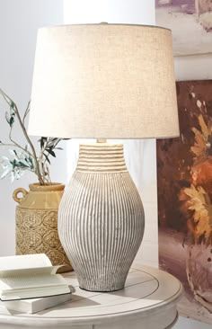 a table with a lamp, vase and book on it next to a wall painting