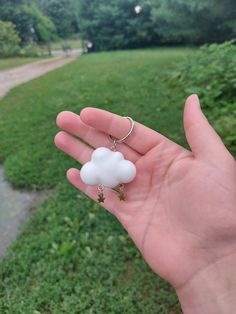 a hand holding a white cloud shaped keychain in front of a grassy area