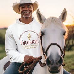 a man in a white hoodie and cowboy hat sitting on top of a horse