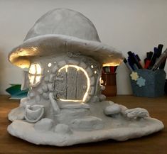 an illuminated mushroom house on top of a wooden table next to pens and pencils