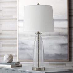 a table lamp with a white shade on it and a painting in the back ground