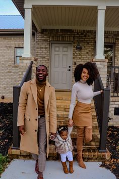 a man and woman holding hands while standing in front of a house with a small child