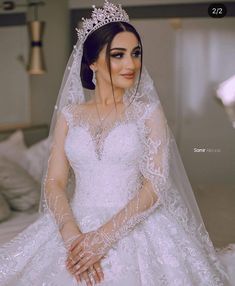 a woman in a wedding dress sitting on a bed wearing a tiara and veil