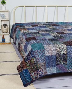 a bed with a blue quilt on top of it next to a white headboard