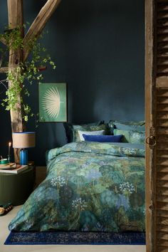 a bedroom with blue walls, green bedding and a plant on the nightstand next to it