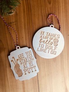 two christmas ornaments hanging from a wooden table with string and twine on it, one is white and the other has brown lettering