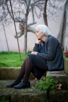 an older woman sitting on steps in front of a tree with her hand under her chin