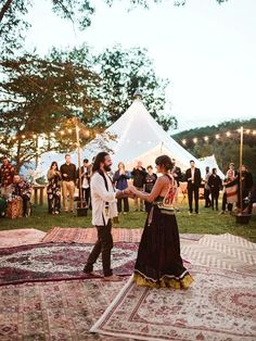 a man and woman dancing on a rug in the middle of a field with people standing around