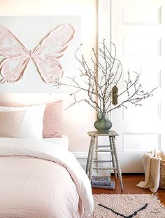 a white bed with pink sheets and pillows next to a painting on the wall above it