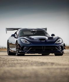 a black sports car parked on top of a dirt field next to a sky background