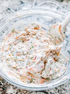 a glass bowl filled with coleslaw on top of a marble counter