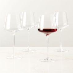 three wine glasses are lined up on a counter top, one is filled with red wine