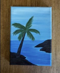 an acrylic painting of a palm tree on a wooden table next to the ocean