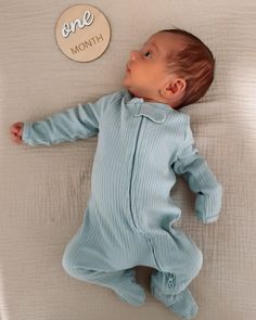 a baby laying on top of a bed next to a one month sign and button