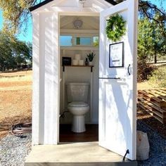 an outhouse with a toilet in it and some plants on the outside door frame