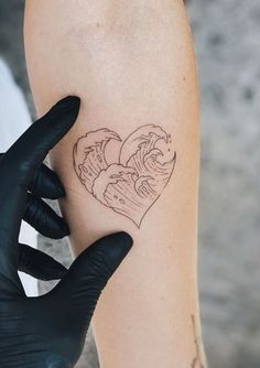 a person with black gloves holding up a tattoo on their left arm that has an image of waves in the shape of a heart