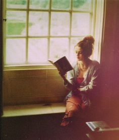 a woman sitting on a window sill reading a book