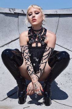 a woman with tattoos on her arm and leg wearing black latex pants sitting down