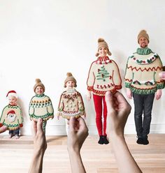 several people are holding small christmas sweaters and dolls in front of a white wall