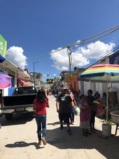 people are walking down the street in front of some shops and vendors on a sunny day