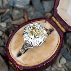 an old - fashioned diamond ring sits in its velvet case on some rocks and stones