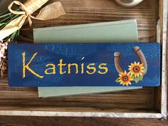 a wooden sign that says katnis with sunflowers and a horseshoe on it