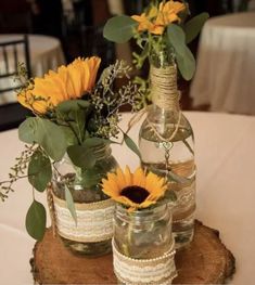 three vases with sunflowers and greenery are sitting on a wood slice