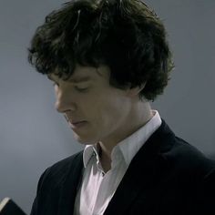 a young man reading a book while wearing a black suit and white collared shirt