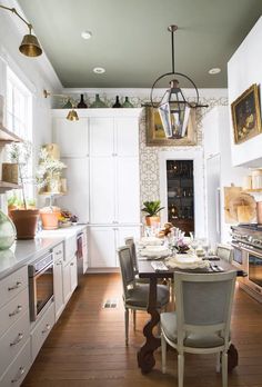 a dining room table and chairs in a kitchen with white cabinets, wood flooring and hanging lights