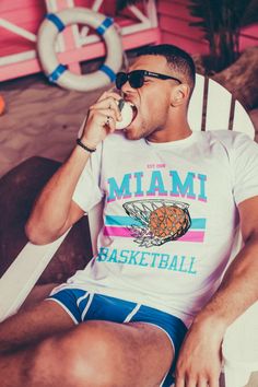 a man sitting in a chair while eating something with his mouth open and sunglasses on