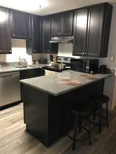 a kitchen with black cabinets and stainless steel appliances in the center island, along with two bar stools