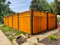 a large wooden fence in the middle of a yard with flowers and trees around it