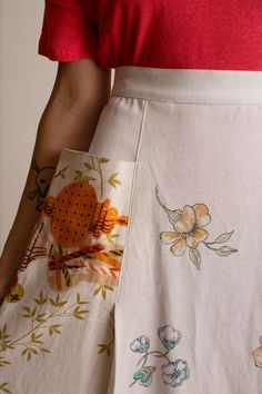 a woman wearing a red shirt and white skirt with floral designs on it's side