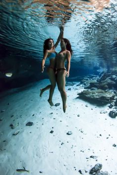 two women in swimsuits under water holding each other's hand and posing for the camera