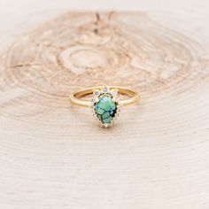 a turquoise stone ring sitting on top of a piece of wood with white diamonds around it